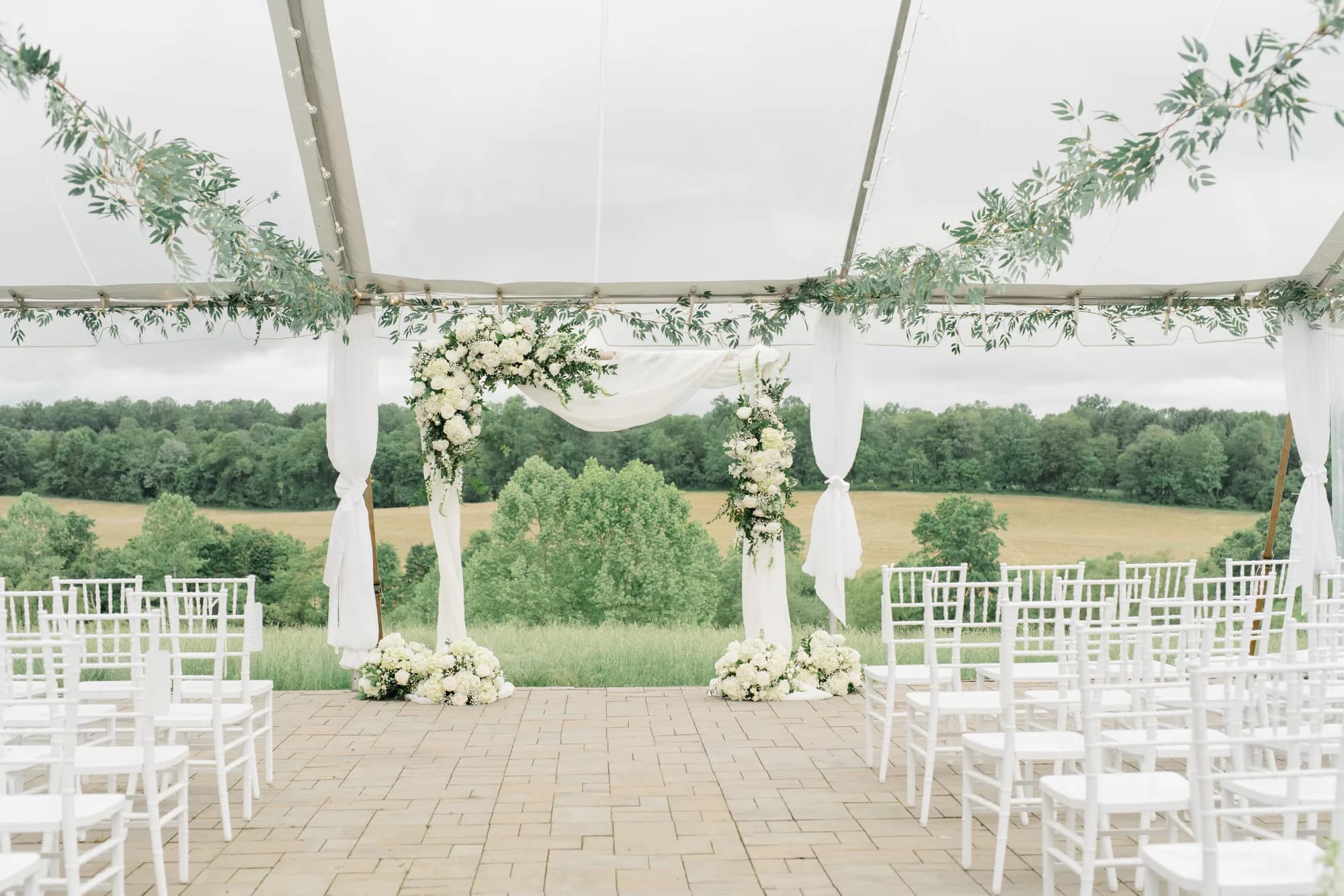 Elegant white floral arch and chiavari chairs under clear tent overlooking Virginia countryside at Rixey Manor