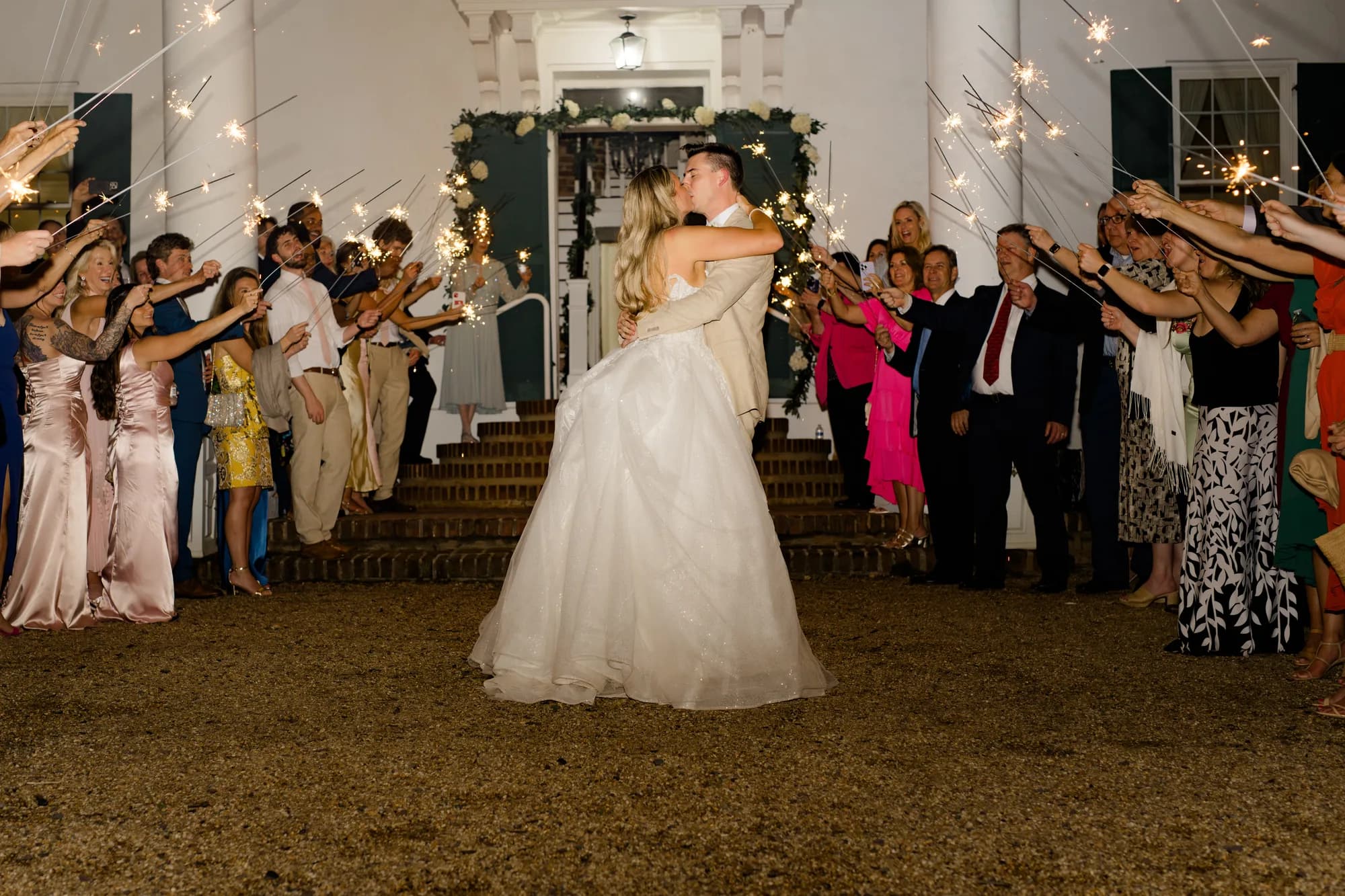 Bride and groom share a kiss during sparkler send-off exit at Rixey Manor's columned entrance at night