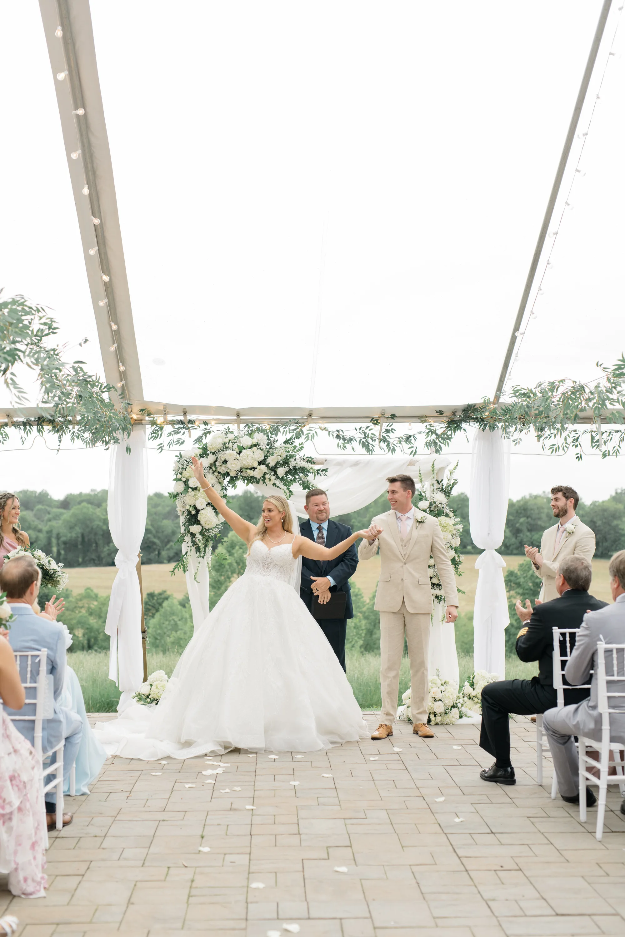 Bride raises arm in joy as newlyweds are announced under Rixey Manor's tent with rolling Virginia fields behind