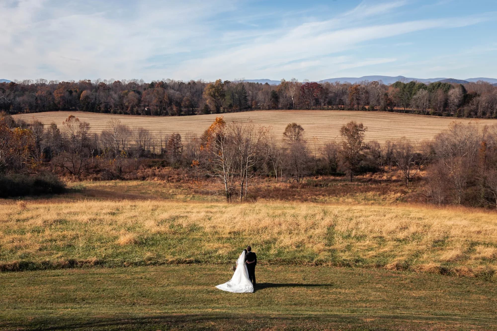 Bride and groom embrace in sweeping autumn fields at Rixey Manor with Blue Ridge Mountains in the distance