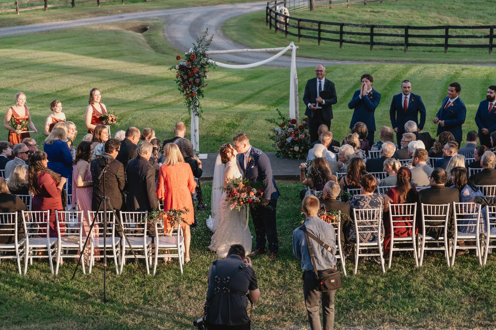 Bride and groom share first kiss at outdoor ceremony on Rixey Manor grounds with rolling hills and fenced pasture behind
