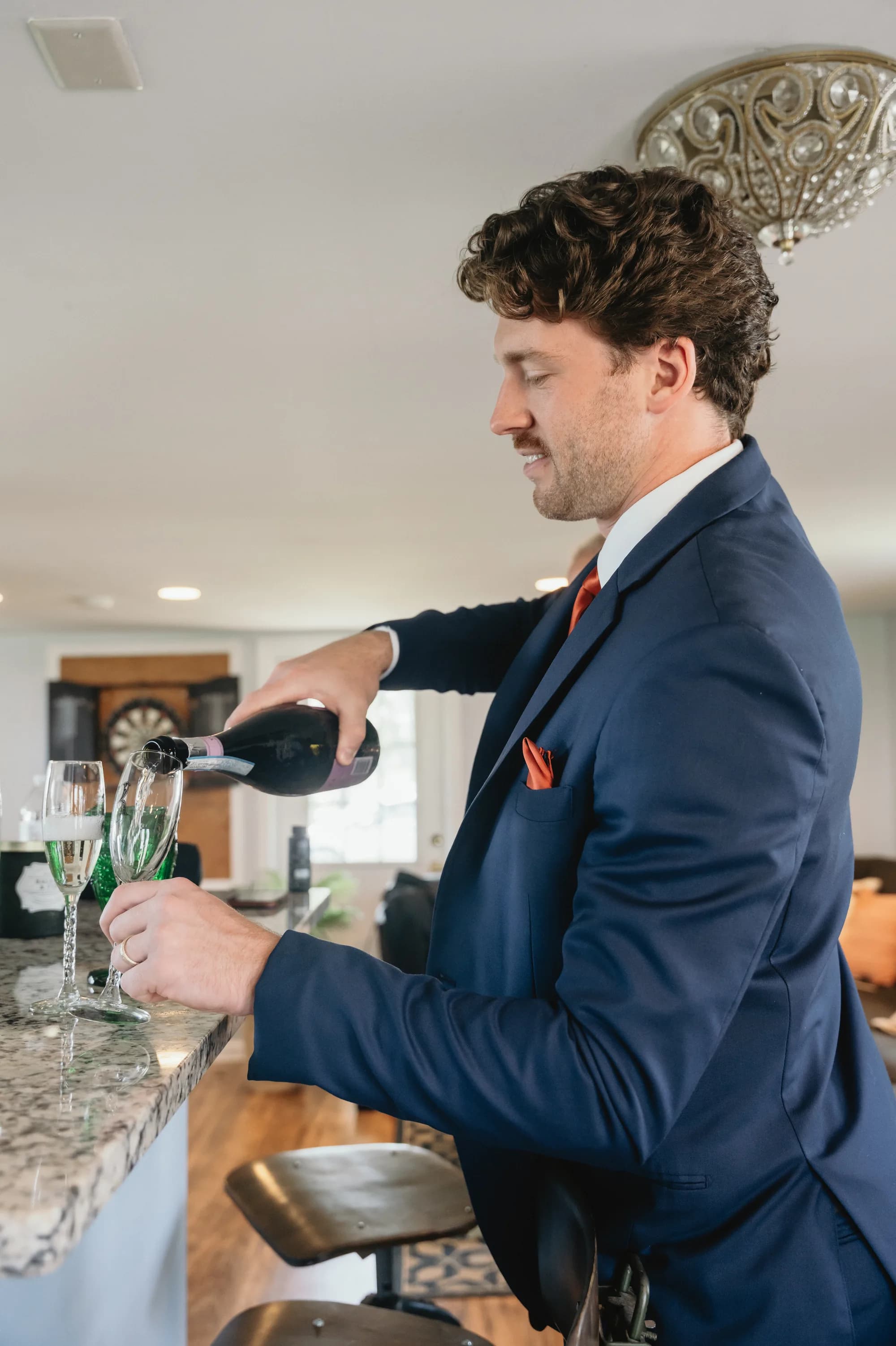 Man in navy suit pouring champagne at bar during wedding preparation