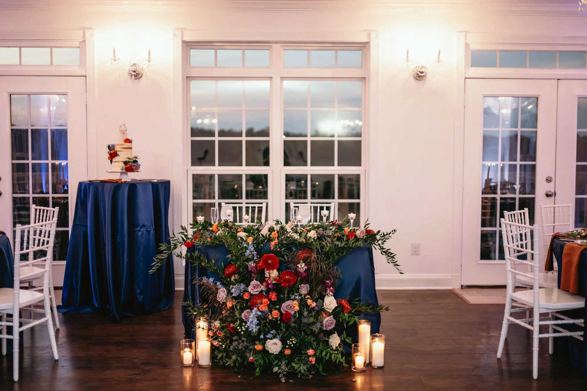 Sweetheart table with lush floral arrangement and candles in Rixey Manor ballroom at twilight