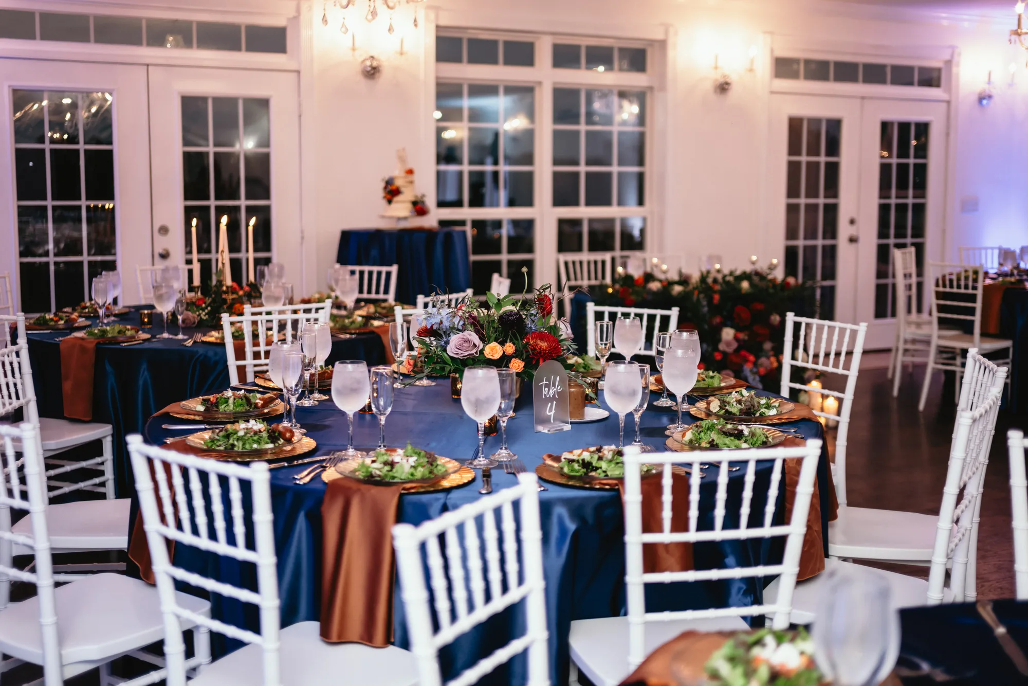 Navy and copper reception tables with floral centerpieces inside Rixey Manor's elegant ballroom at night