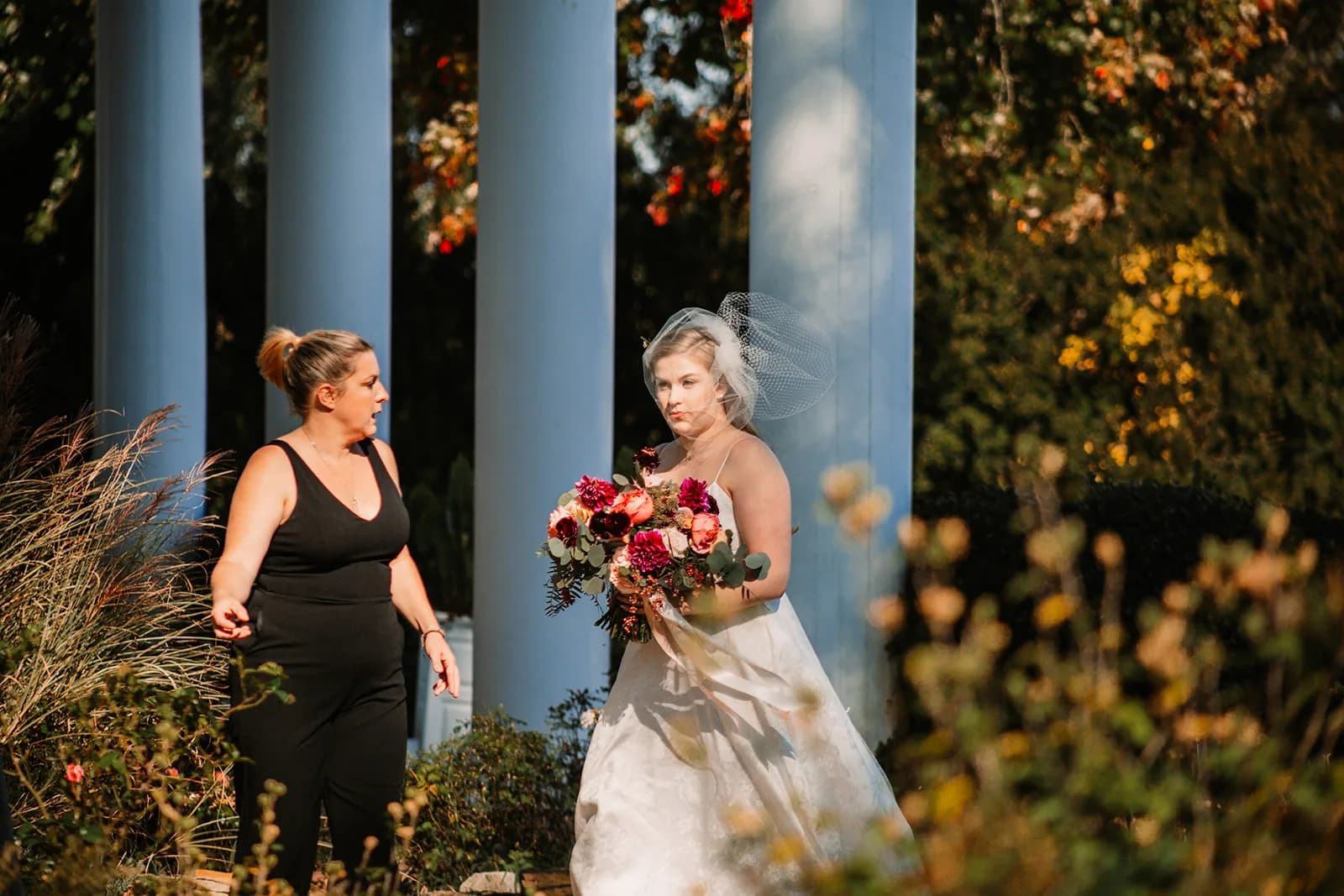 Bride in white dress with bouquet poses with bridesmaid in black at Rixey Manor columns