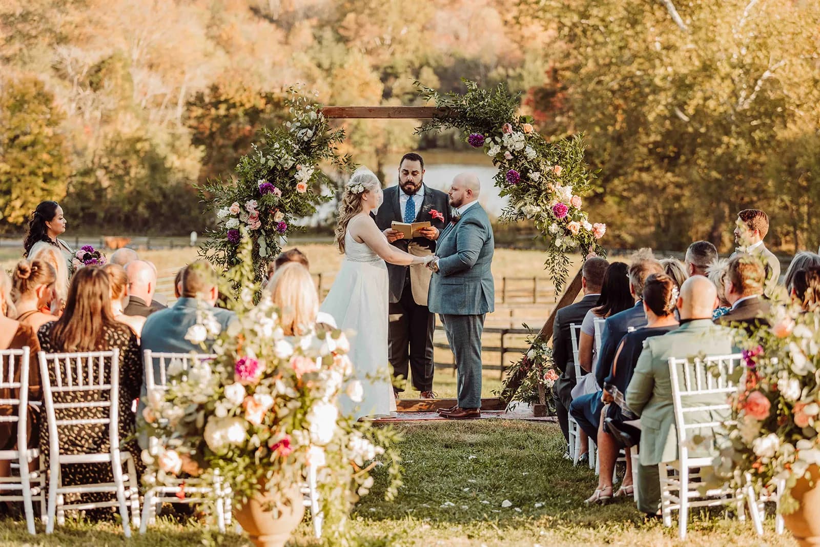 Couple exchanging vows under floral arch at Rixey Manor outdoor ceremony with fall foliage backdrop