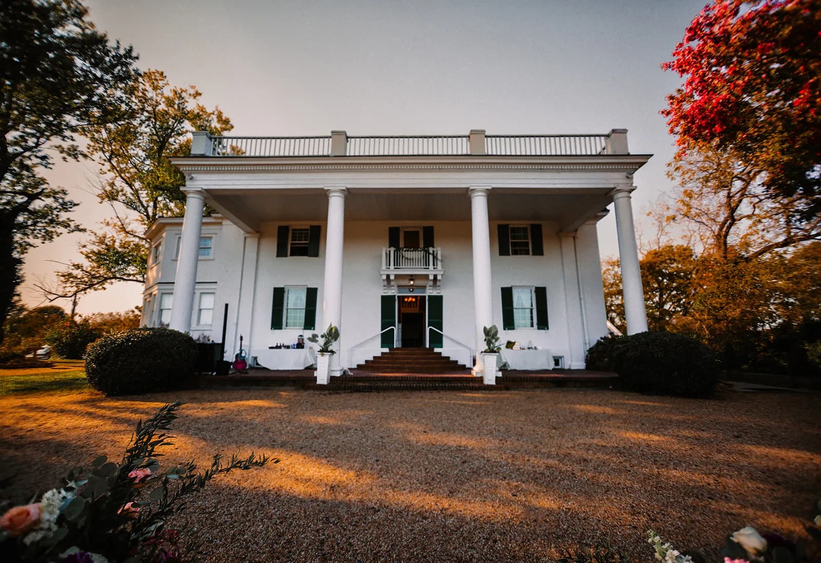 White columned manor house at golden hour with autumn foliage and manicured grounds