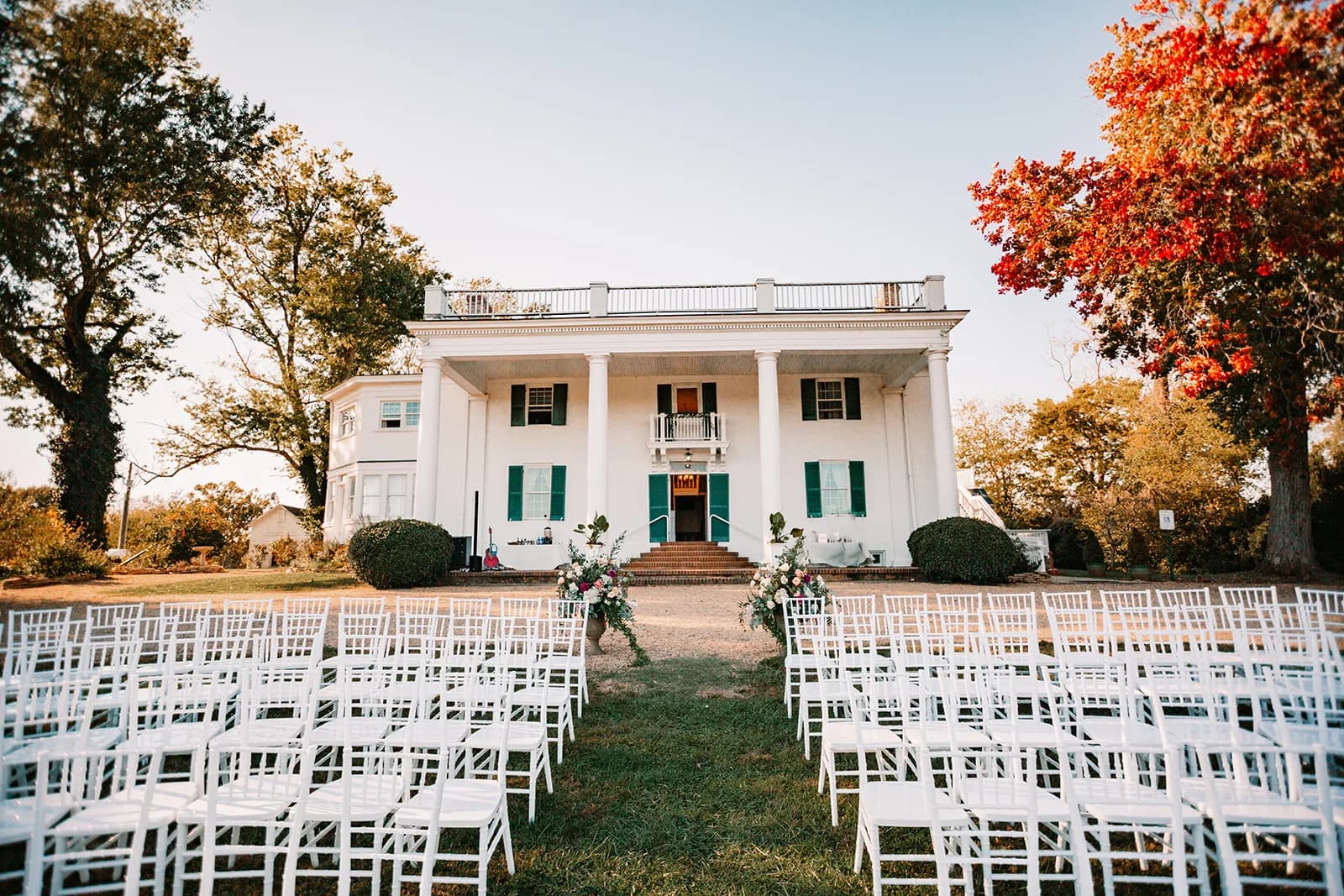 Rows of white chairs line the aisle before Rixey Manor's white-columned facade amid autumn foliage