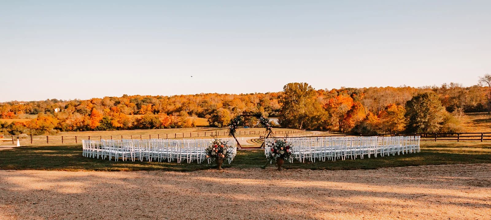 Outdoor ceremony setup with white chairs and floral arch surrounded by vivid autumn foliage at golden hour in rural Virginia