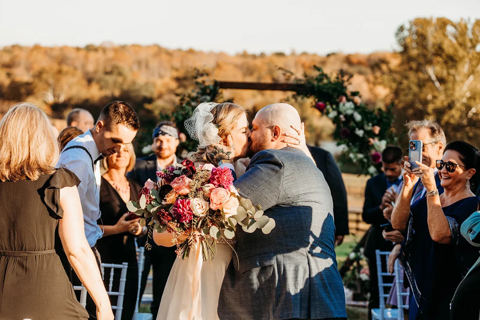 Bride and groom share first kiss while walking the aisle at Rixey Manor outdoor ceremony with floral arch