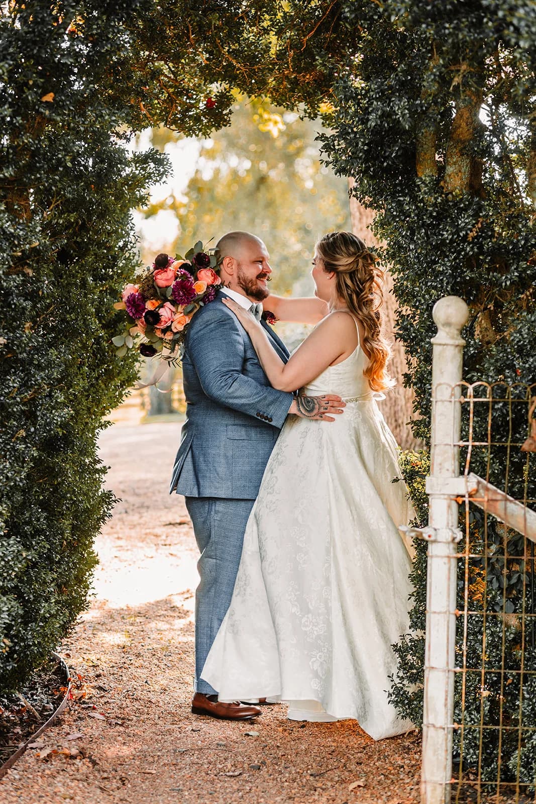 Bride and groom share a joyful moment framed by a lush hedge archway and iron gate at Rixey Manor