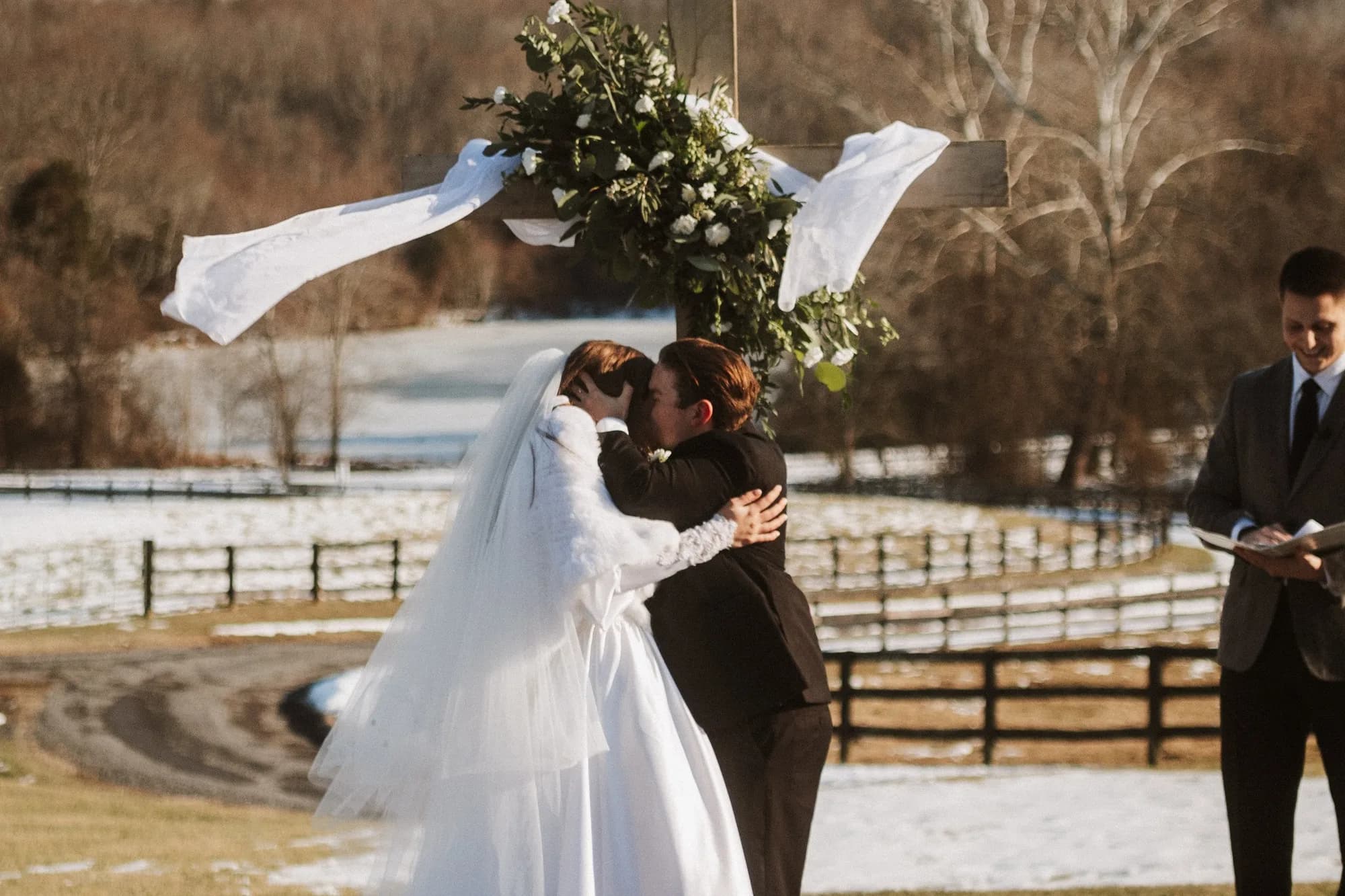 Bride and groom share first kiss at outdoor winter ceremony at Rixey Manor, snow-covered Virginia countryside behind them