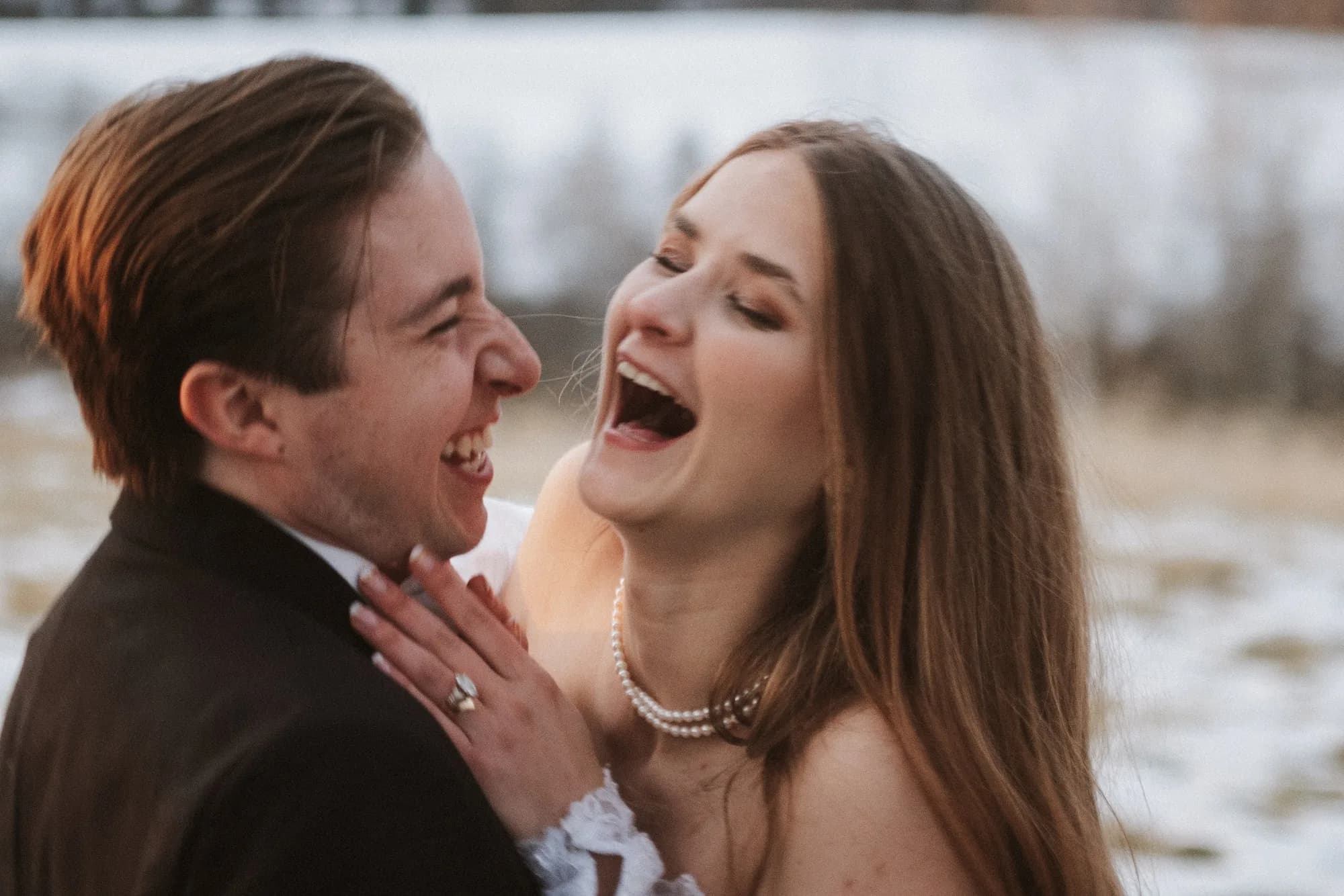 Bride and groom laughing joyfully together outdoors in winter, bride in pearl necklace and strapless gown