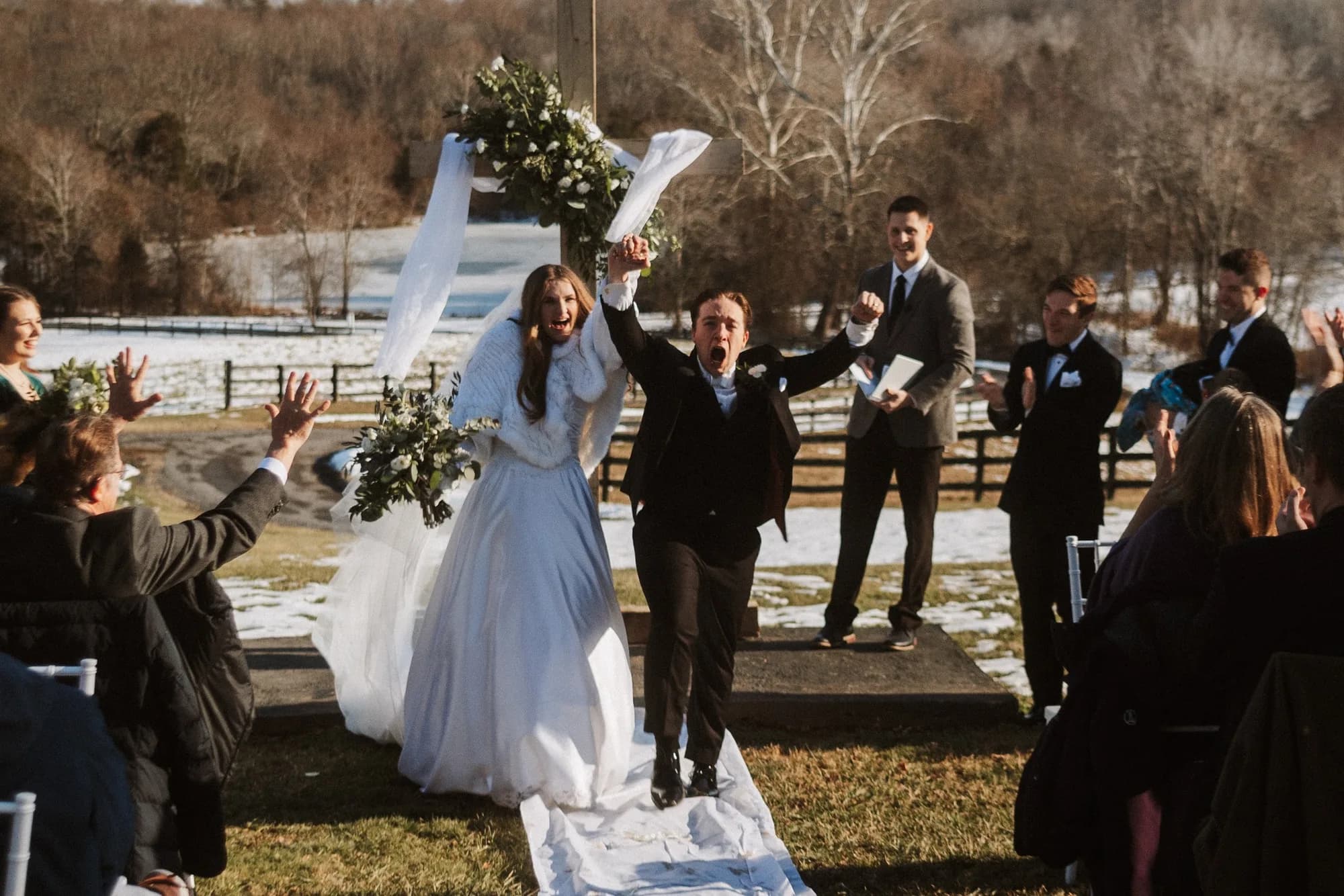 Bride and groom cheer exuberantly as they walk back down the aisle at a snowy outdoor Rixey Manor winter ceremony