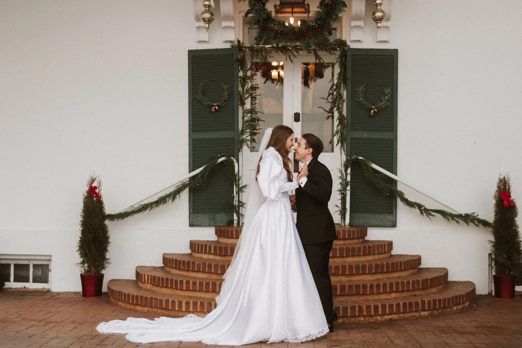 Bride and groom share a tender moment on the brick carriage steps at Rixey Manor, adorned with holiday greenery.