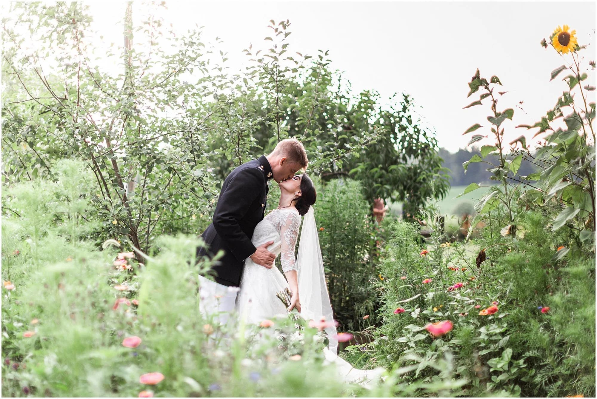 Bride and groom share a kiss surrounded by wildflowers and sunflowers in a lush garden setting