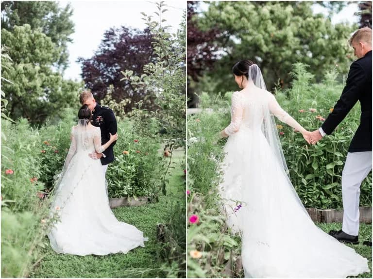 Bride and groom walk hand-in-hand through lush garden greenery, bride's long veil trailing behind