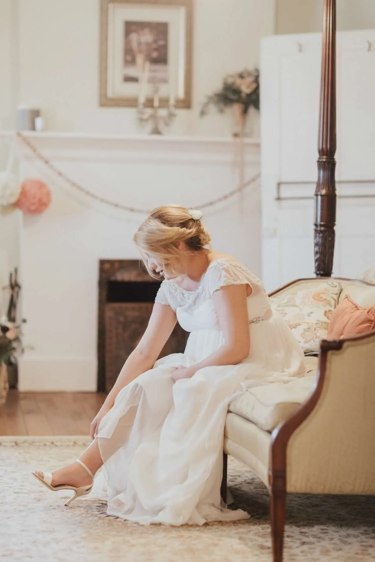 Bride smiling as she fastens her heels in a softly lit vintage room before her wedding ceremony