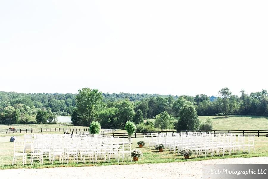 Outdoor ceremony setup with white chairs and floral arrangements overlooking green Virginia countryside at Rixey Manor