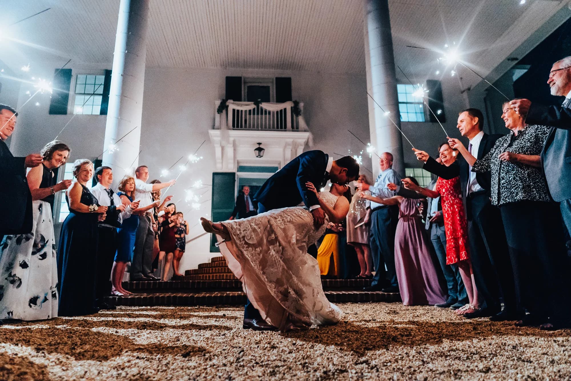 Groom dips bride in romantic kiss during sparkler send-off outside Rixey Manor's white columned entrance at night
