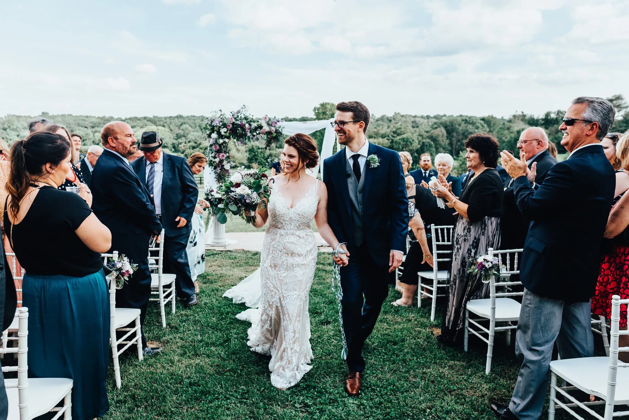 Bride and groom walk back up the aisle at Rixey Manor outdoor ceremony as guests cheer and applaud