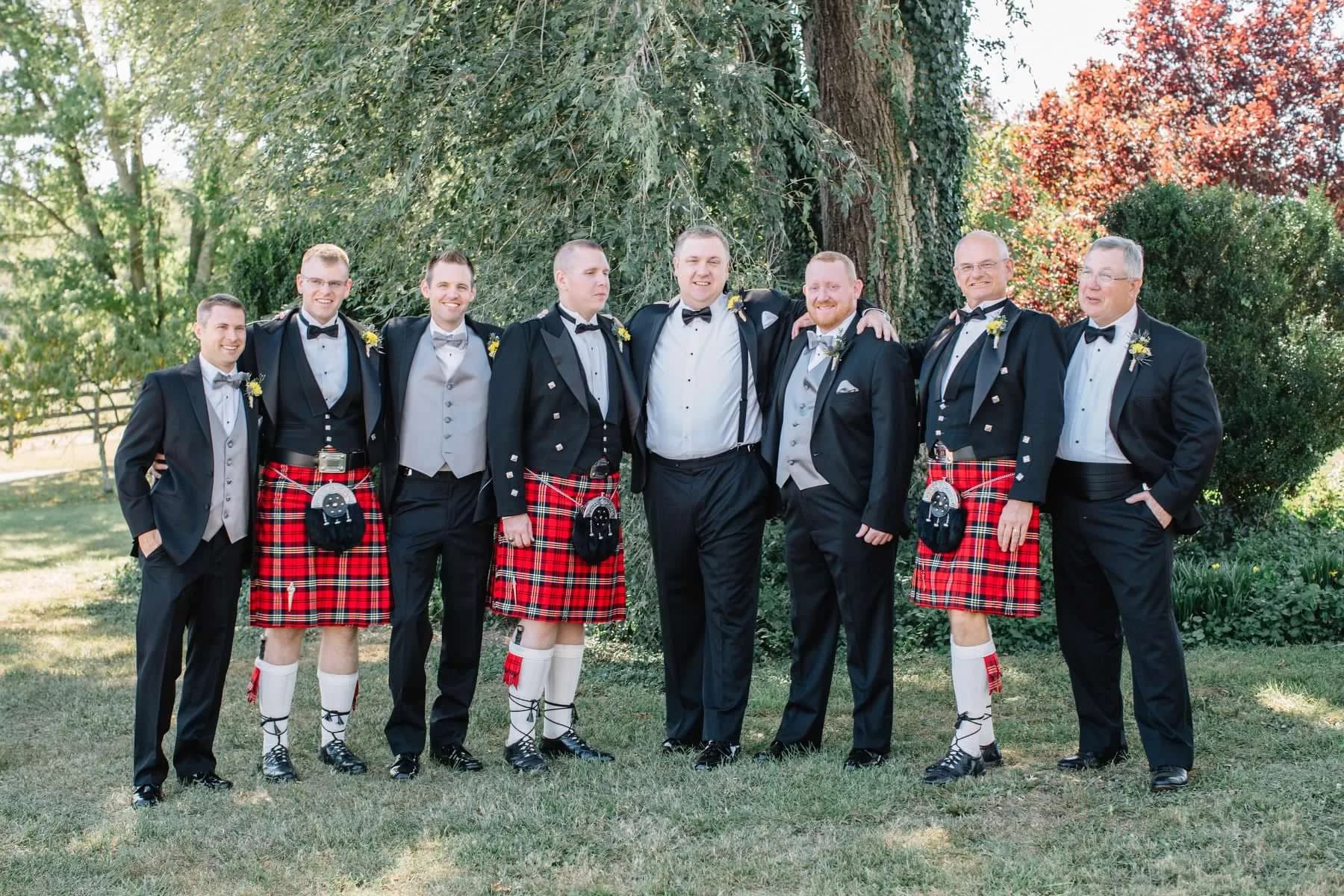 Groomsmen in kilts and tuxedos laughing together on the grounds of Rixey Manor