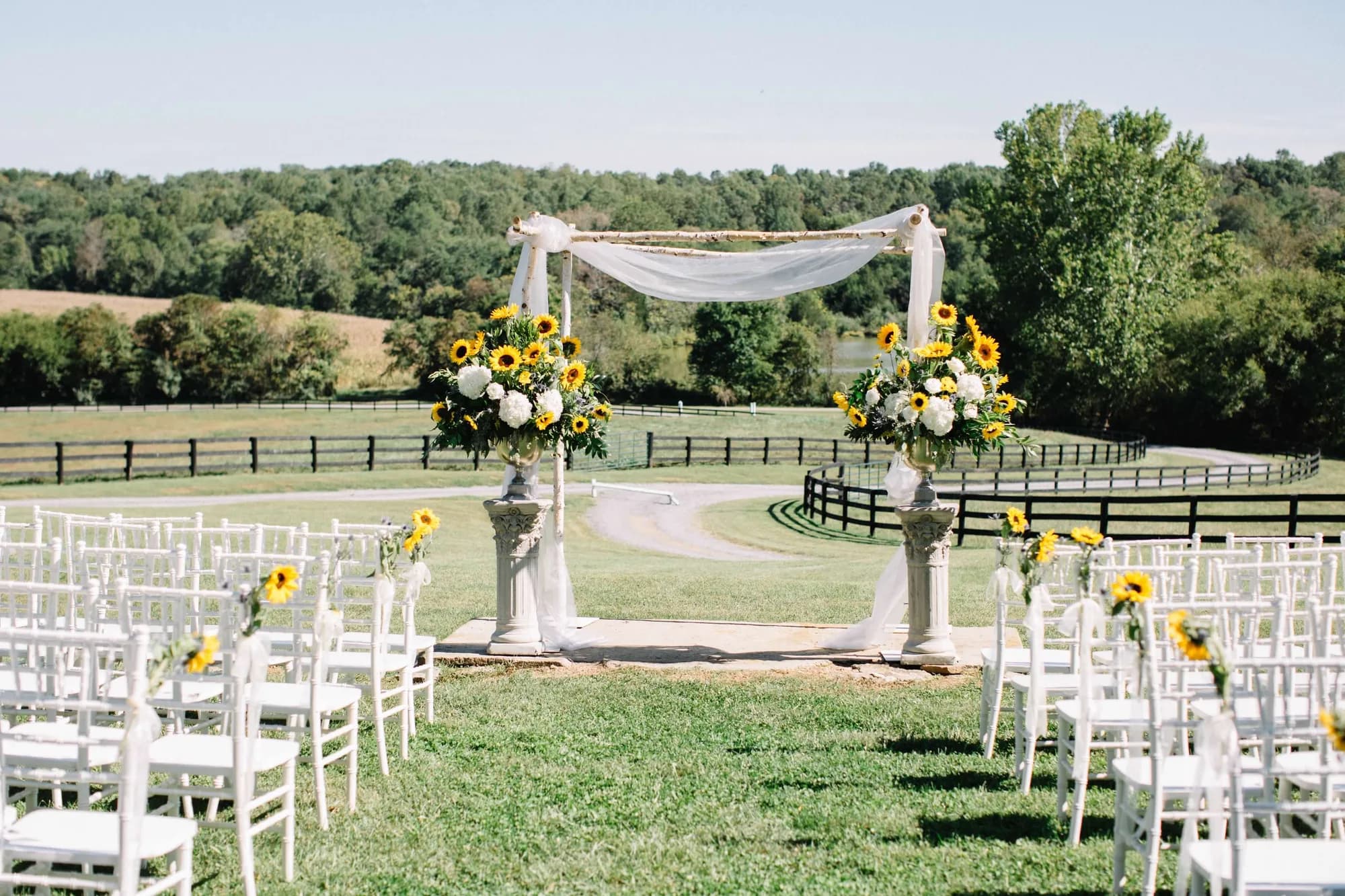 Sunflower-adorned outdoor ceremony arch at Rixey Manor with white chairs and rolling Virginia countryside backdrop