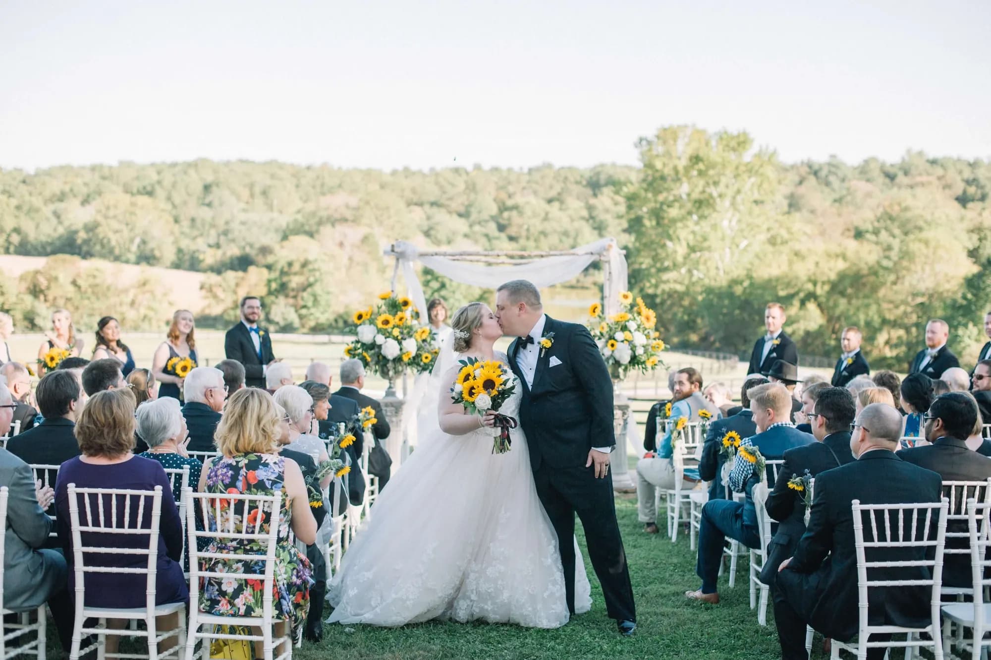 Bride and groom share first kiss at outdoor Rixey Manor ceremony with sunflower arch and rolling Virginia hills behind them