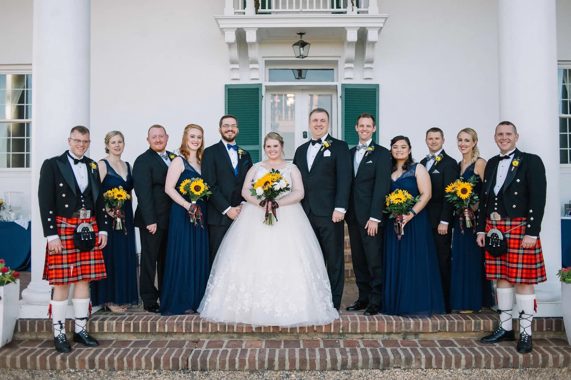Wedding party in kilts and navy gowns pose with couple on steps of Rixey Manor's white columned entrance