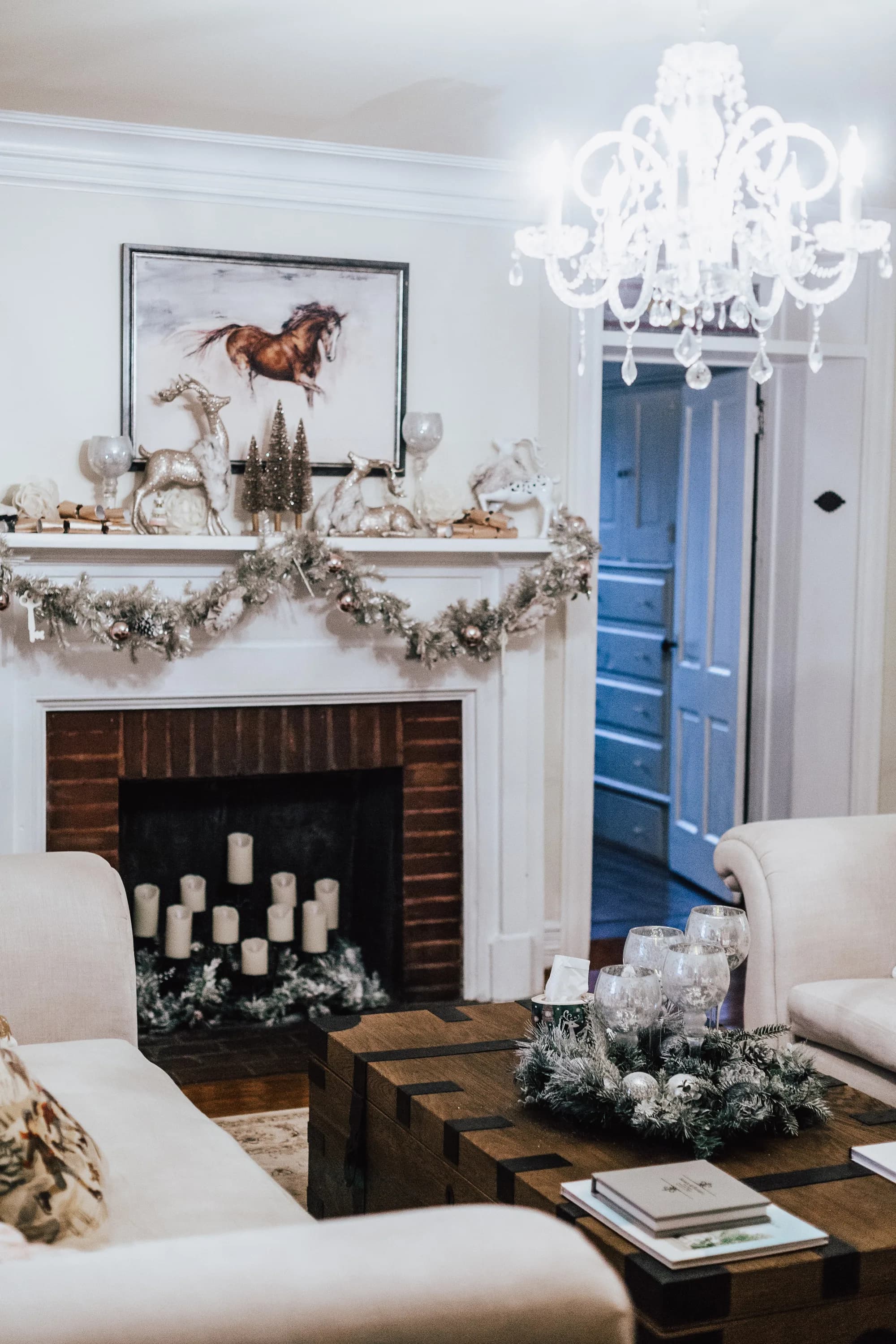 Elegant holiday-decorated living room with white fireplace, crystal chandelier, and horse painting at Rixey Manor