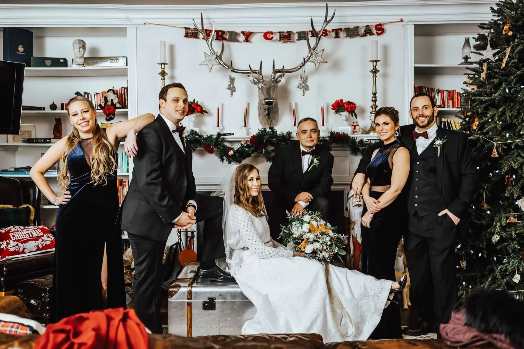 Formal wedding party portrait in elegant Christmas-decorated manor library with bride, groom, and wedding party in black attire