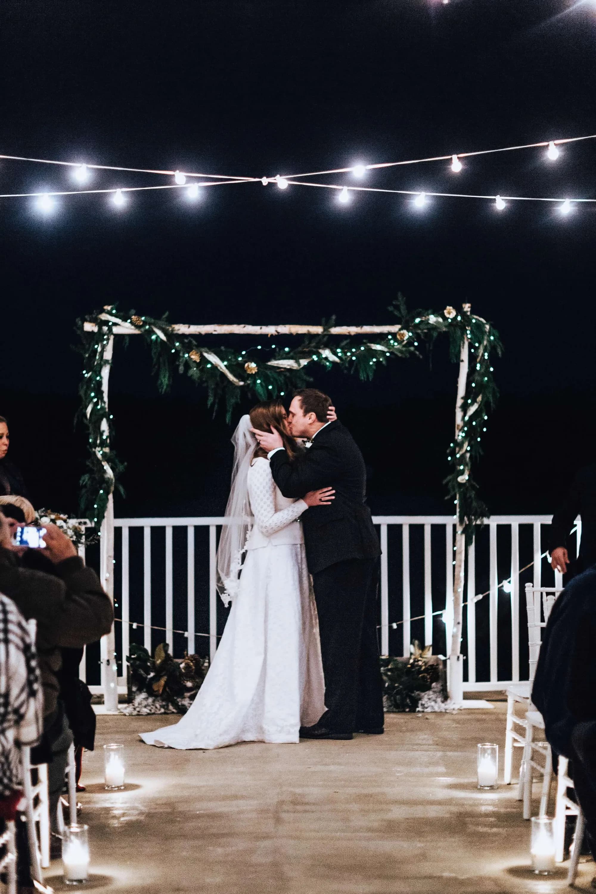 Bride and groom share first kiss under a floral arch on Rixey Manor's candlelit outdoor terrace at night