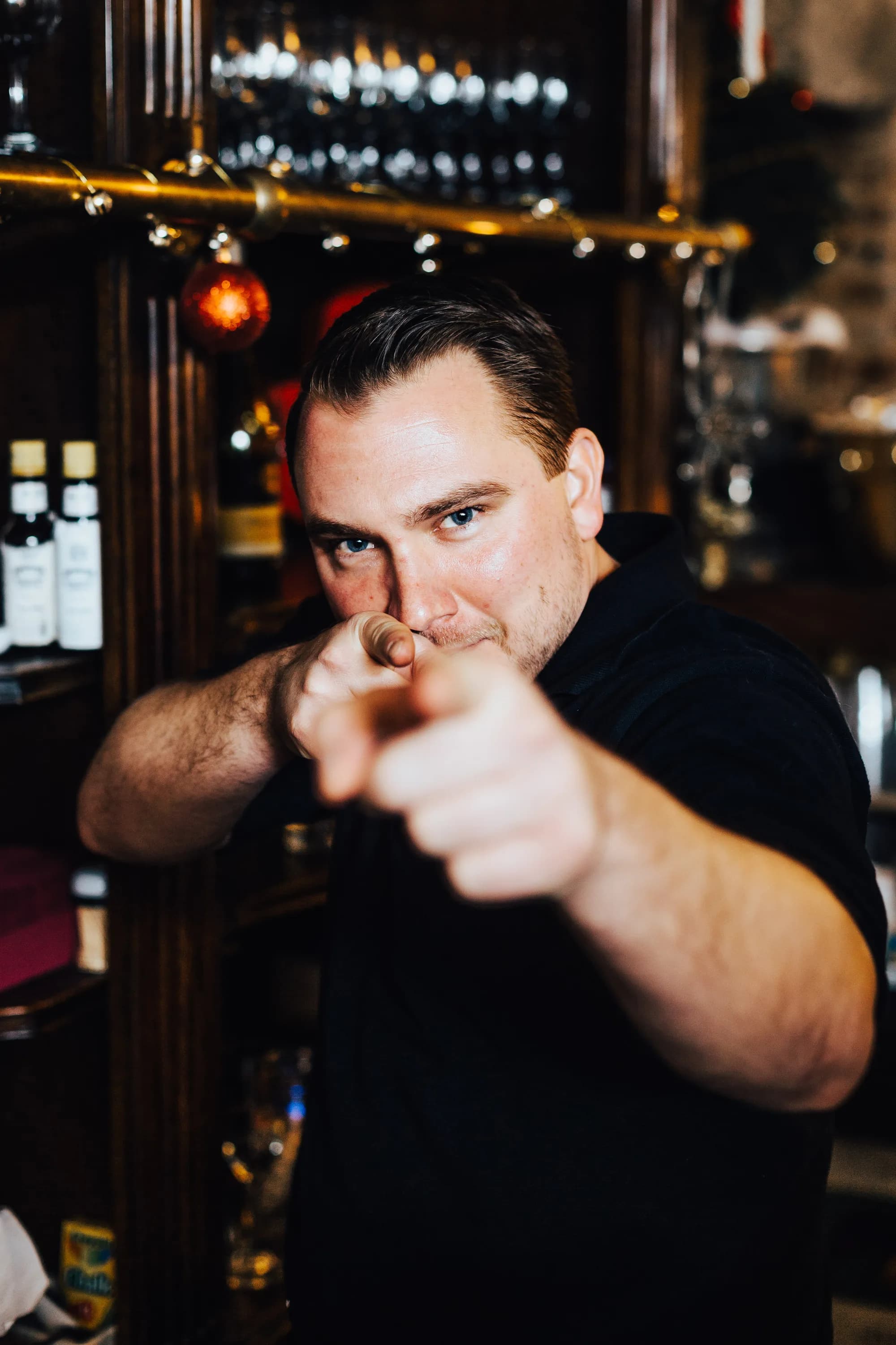 Man in black shirt pointing at camera in front of illuminated venue backdrop