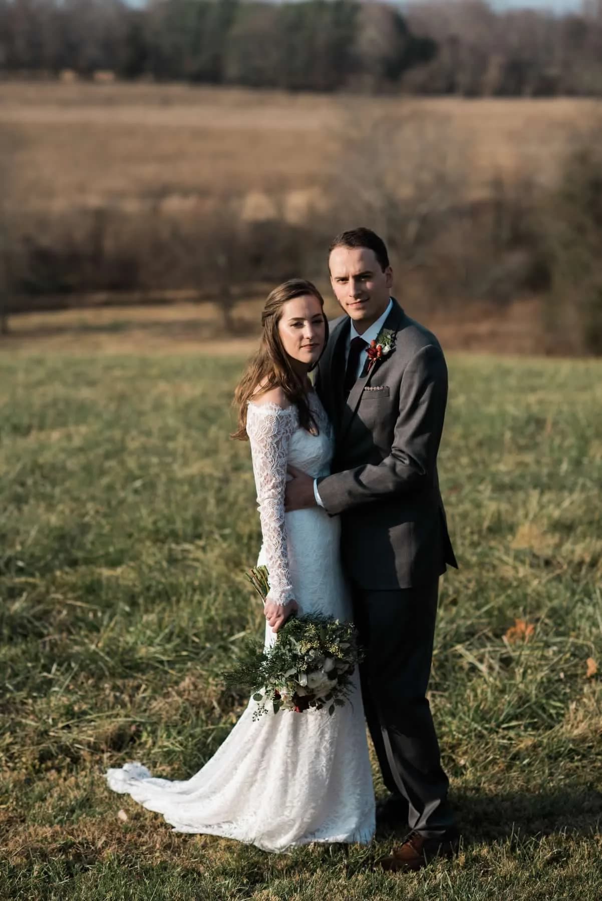 Bride and groom embrace in golden-hour field at Rixey Manor, she holds lush greenery bouquet, rolling Virginia countryside behind them.