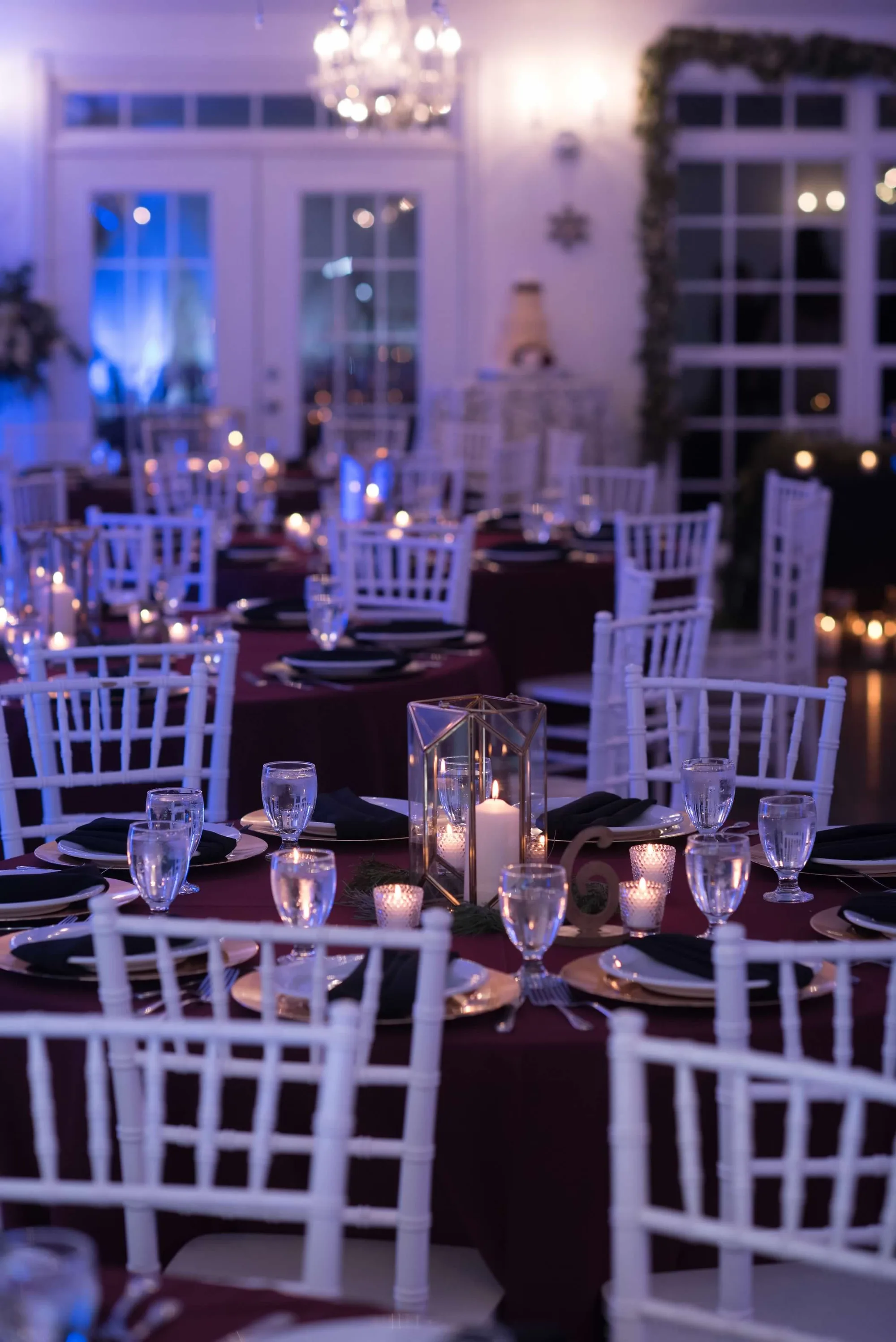 Candlelit reception tables with burgundy linens and white chiavari chairs in the Rixey Manor ballroom