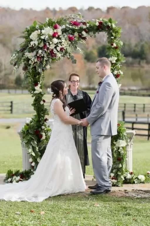 Bride and groom exchange vows under floral arch at Rixey Manor with rolling Virginia countryside behind them