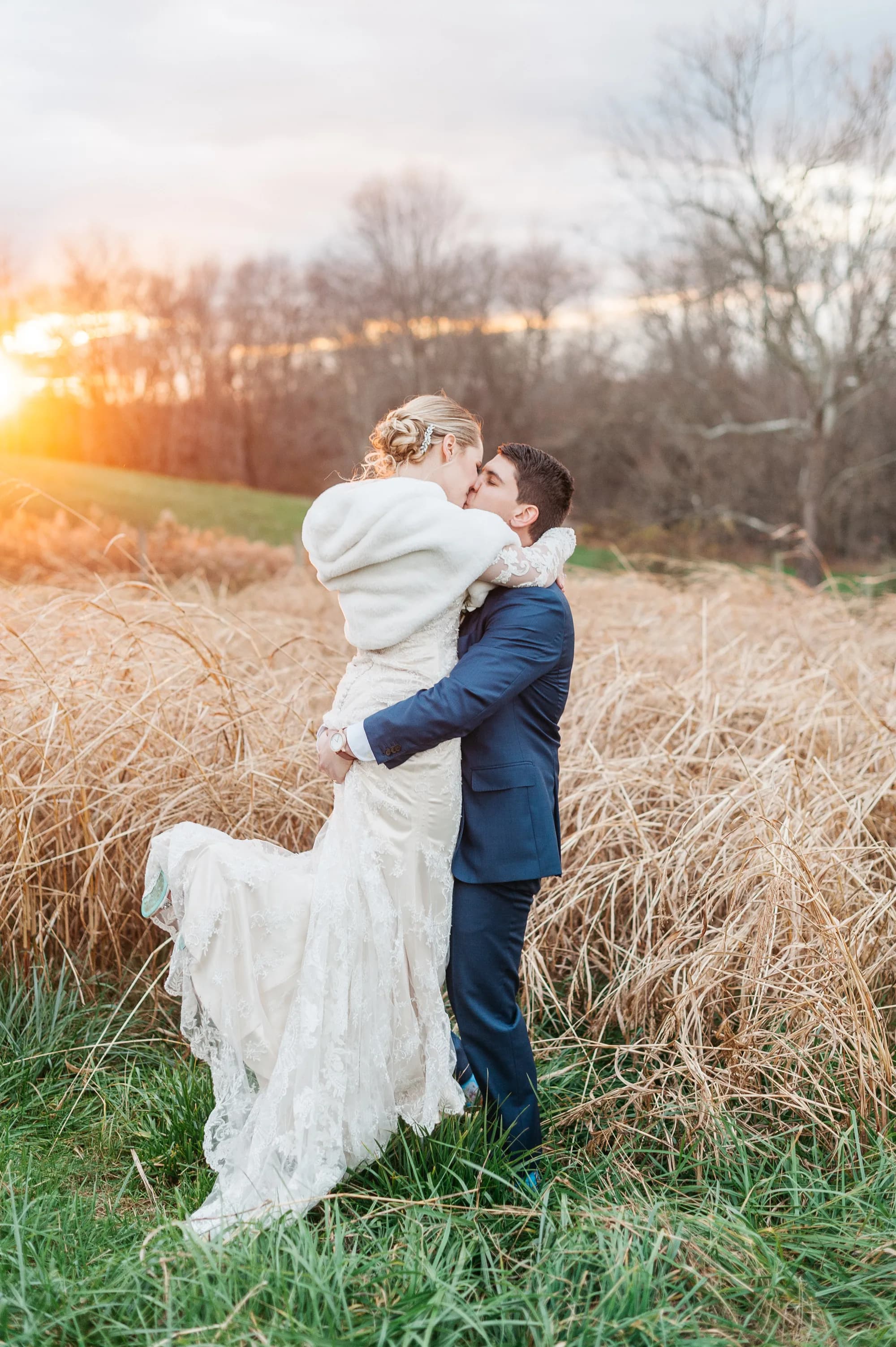 Groom lifts bride for a kiss at golden hour in a field of tall grass at Rixey Manor