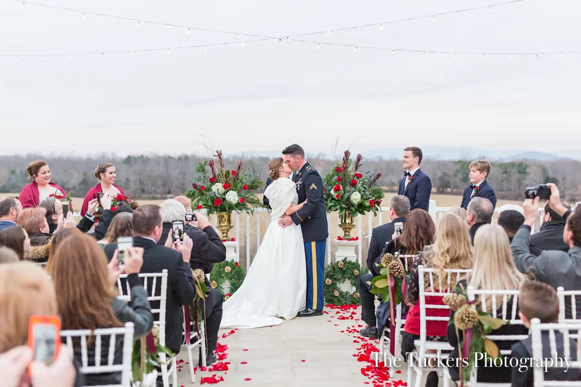Military groom and bride share first kiss at outdoor Rixey Manor ceremony with rose petal aisle and mountain views
