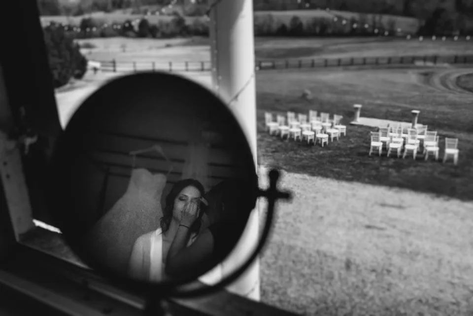 Bride reflects in vanity mirror overlooking Rixey Manor's ceremony chairs set on rolling Virginia countryside