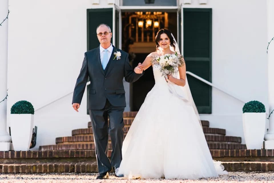 Bride and father walk down Rixey Manor's brick carriage steps in bright winter light, bride holding white bouquet.