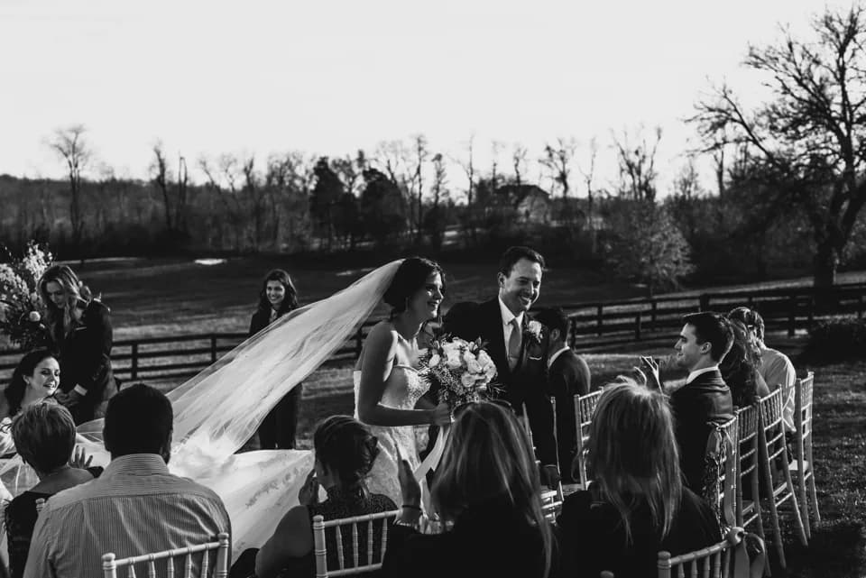 Laughing bride and groom walk the aisle at outdoor Rixey Manor ceremony with pastoral Virginia countryside behind them