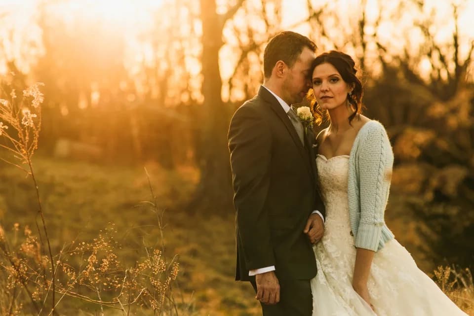 Bride and groom in golden sunset light among dried plants in rural field