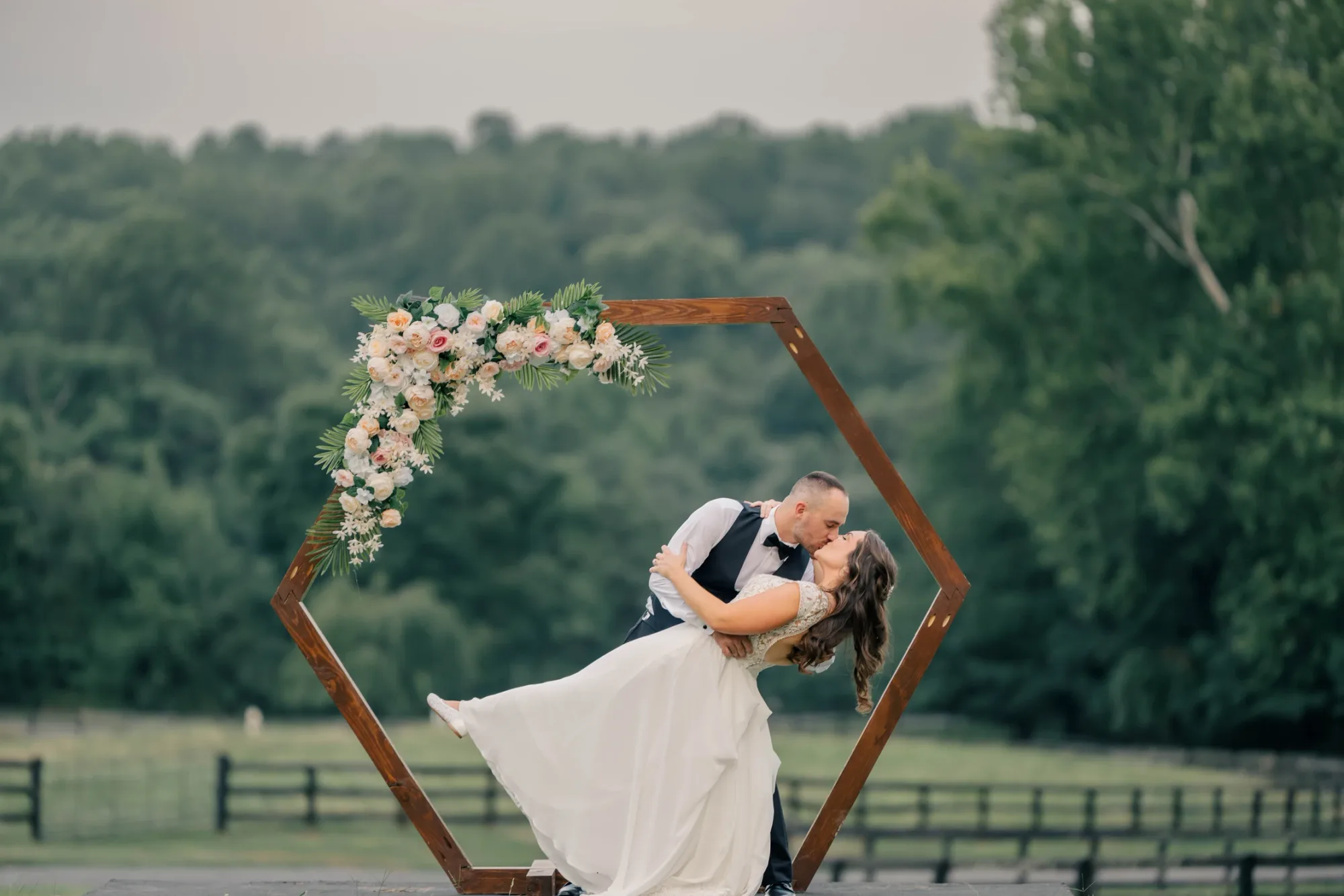 Groom dips bride in a kiss before a floral hexagon arch at Rixey Manor's lush green estate grounds