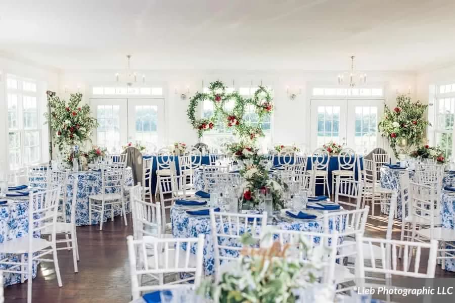Sunlit Rixey Manor ballroom with blue floral tablecloths, white chiavari chairs, and greenery wreaths on windows