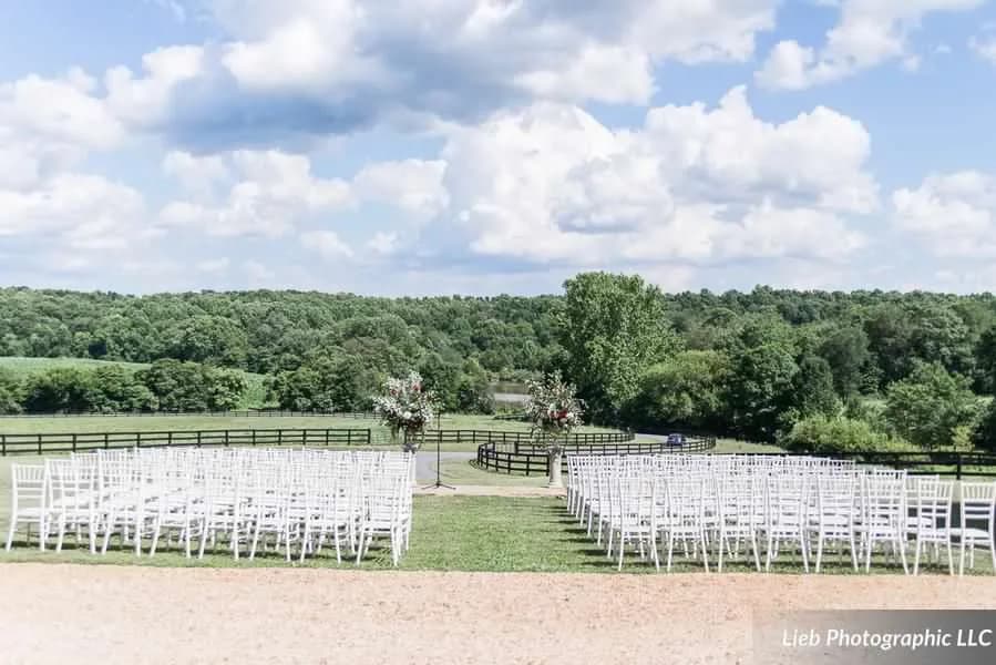Outdoor wedding ceremony setup with white chiavari chairs flanking a floral arch overlooking rolling Virginia hills
