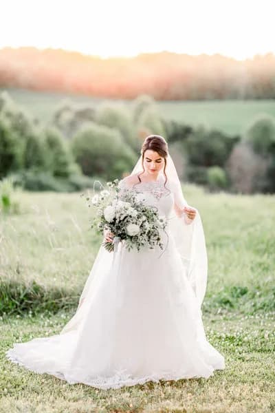 Bride in ballgown holds white floral bouquet on golden-hour meadow at Rixey Manor Virginia estate