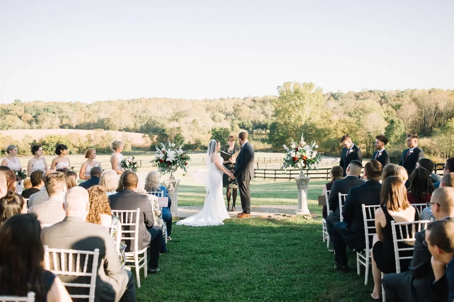 Couple exchanging vows at outdoor ceremony on Rixey Manor's rolling Virginia countryside lawn at golden hour
