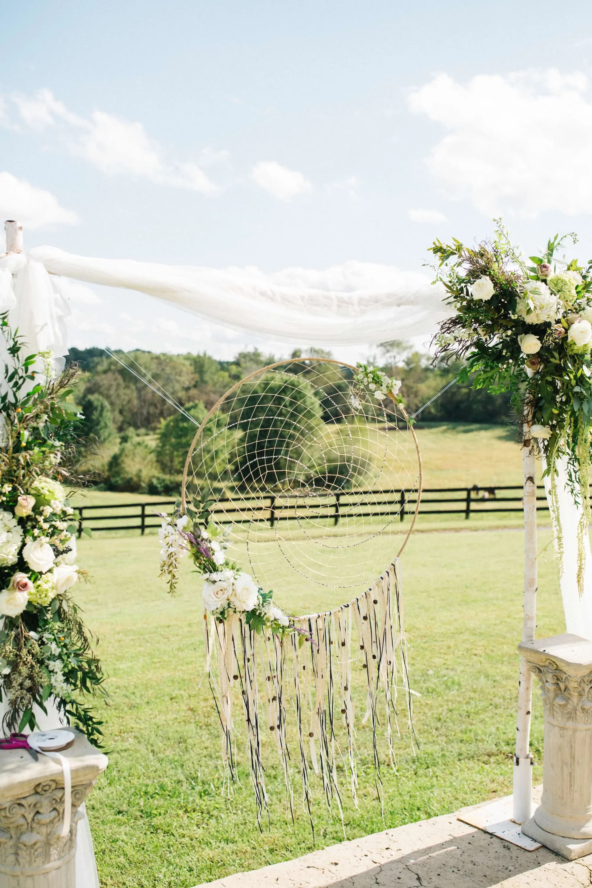 Boho dreamcatcher ceremony backdrop with white florals at Rixey Manor's outdoor ceremony site overlooking green pastures