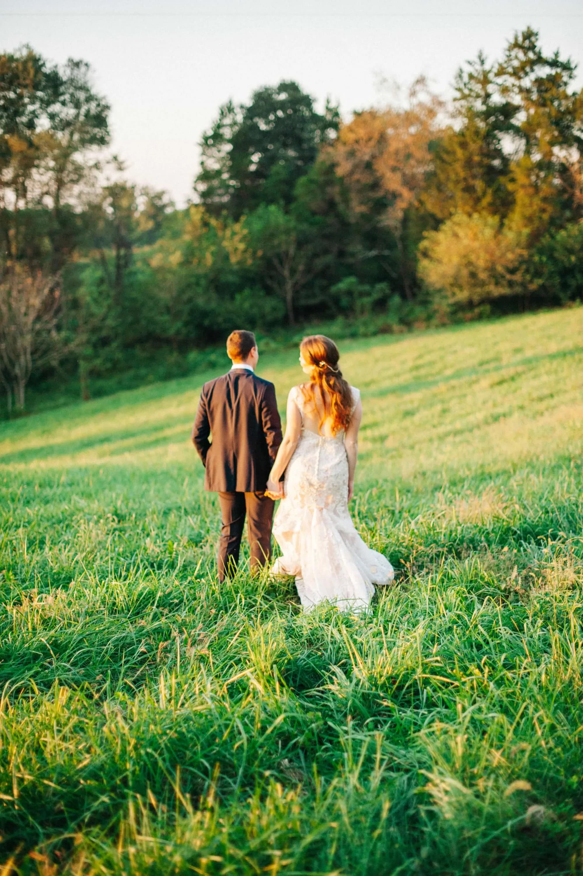 Bride and groom walking hand-in-hand through lush green meadow at golden hour at Rixey Manor