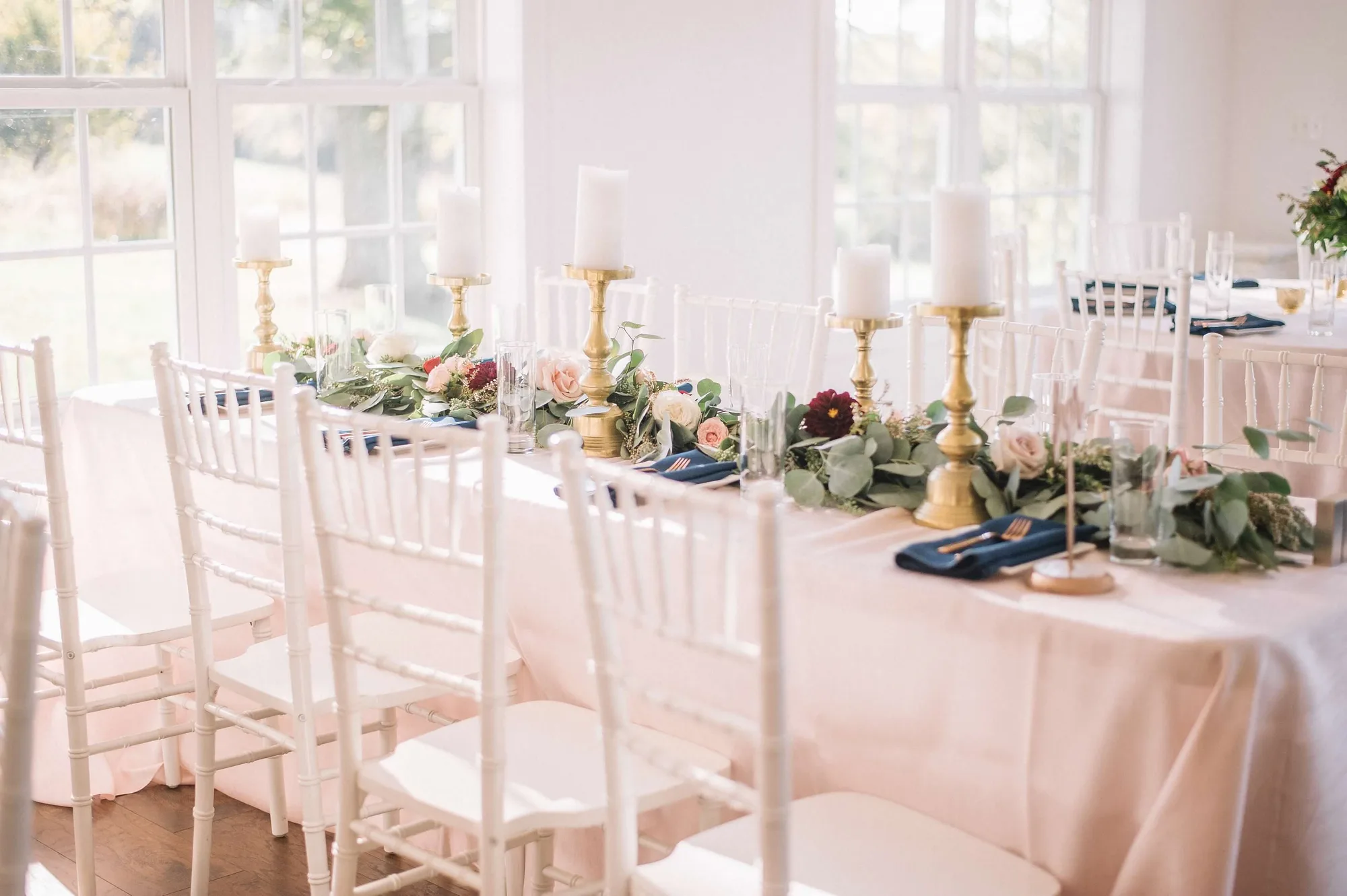 Elegant reception table with gold candelabras, greenery garland, and navy napkins in a bright Rixey Manor event space